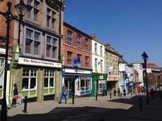 people are walking down the sidewalk in front of shops and businesses on a sunny day