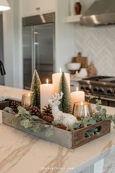 candles are placed in a tray on the kitchen counter with pine cones and evergreens