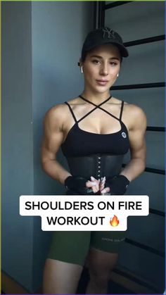 a woman in black top and green shorts standing next to wall with text that reads shoulders on fire workout