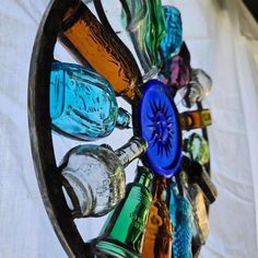 there are many different colored glass bottles in the wheel on this wall hanging decoration that is made out of wood and metal