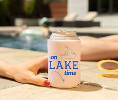 a woman's hand holding a can of lake time next to a swimming pool