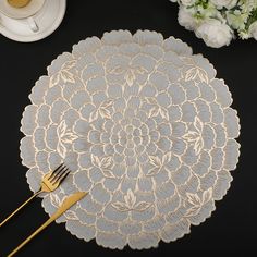 a table setting with silverware and white flowers on the black table cloth, along with a gold fork and knife