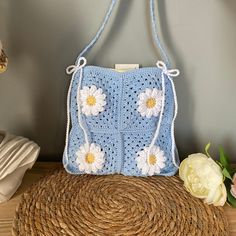 a blue crocheted purse sitting on top of a straw hat next to flowers