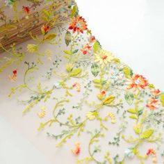 a piece of fabric with flowers and leaves embroidered on it, next to a roll of thread