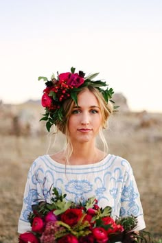 a woman with flowers in her hair holding a bouquet of red roses and greenery