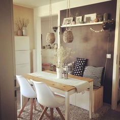 a dining room table with white chairs in front of a gray wall and hanging decorations