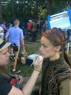 a woman is getting her makeup done at an outdoor event with other people in the background