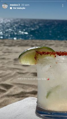 a close up of a drink on a table near the water and sand with an ocean in the background