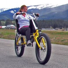 a woman riding a yellow bike down a road next to mountains and trees in the background