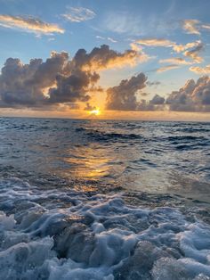 the sun is setting over the ocean with waves coming in to shore and clouds above