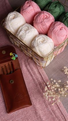 several balls of yarn sitting in a basket next to a leather case