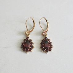 Thousands of years ago red garnet was considered to be one of the most prized possessions for Egyptian pharaohs, these beautiful gems then became popular with clergy and nobility in Rome. This rich history gives garnet a beautiful allure and makes a great gift! These 14k gold earrings are set with pear shaped garnets in a halo of round garnets that dangle from the lever back settings. Metal: 14K Yellow Gold Garnet Pear: 7 x 5 MM Garnet Rounds: 2.3 MM Length: 1 Inch Width .5 Inch For a greater se Yellow Gold Garnet Round Earrings, Classic Burgundy Jewelry For Wedding, Antique Garnet Birthstone Jewelry, Traditional Oval Red Earrings, Elegant Garnet Teardrop Earrings, Elegant Garnet Drop Earrings, Elegant Pierced Garnet Earrings, Traditional Red Oval Earrings, Classic Ruby Jewelry In Burgundy