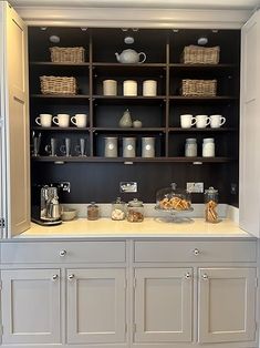 a kitchen with white cupboards and shelves filled with coffee pots, teapots and other items