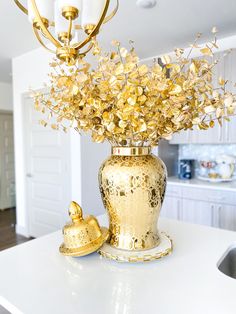 a gold vase filled with lots of flowers on top of a white kitchen countertop