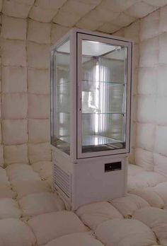 a white display case sitting inside of a room filled with mattresses and pillows on the floor