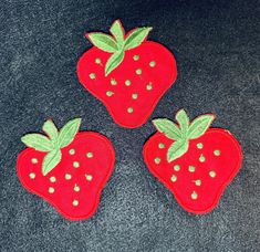 three red strawberry appliques with green leaves on black carpeted area, top view