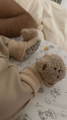 a teddy bear laying on top of a bed next to a person's feet