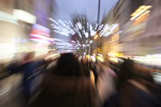 blurry photograph of people walking down the street at night time with lights in the background