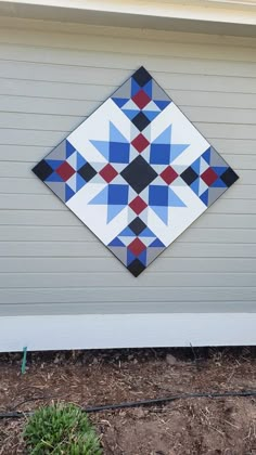 a blue, red and black quilt hanging on the side of a house's wall