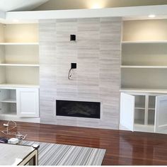 an empty living room with white bookcases and a fireplace in the center,