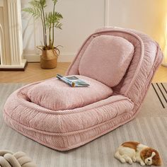 a dog laying on the floor next to a pink chair with a book on it