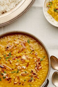 there is a bowl of food on the table with rice and spoons next to it