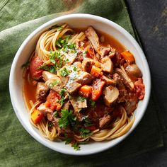 a white bowl filled with pasta and meat on top of a green cloth next to a fork