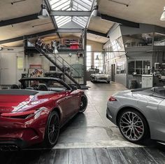 two sports cars parked in a garage with stairs leading up to the second floor and another car on the other side