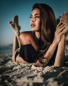 a woman laying in the sand with her hands on her chest