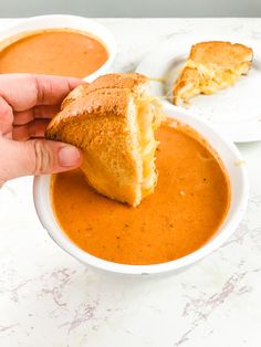 a hand holding a piece of bread over a bowl of soup