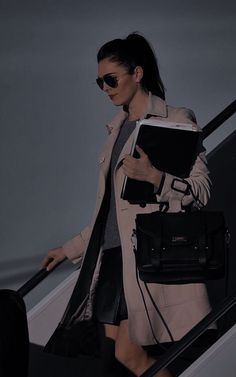 a woman is walking down an escalator carrying a book and purse in her hand