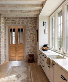 a kitchen with stone walls and wooden floors, along with an open door leading to the outside