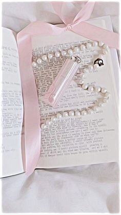 an open book with pearls and a pink ribbon