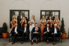 a group of people in suits and ties posing for a wedding photo with their bouquets