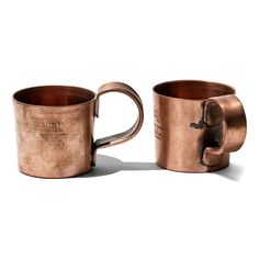 two copper mugs sitting side by side on a white surface