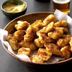 a wooden bowl filled with fried food on top of a table next to a glass of beer