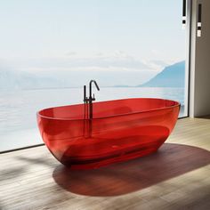 a red bathtub sitting on top of a wooden floor next to a large window