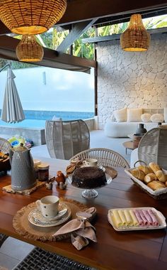 a table with food and drinks on it next to the ocean in front of an open window