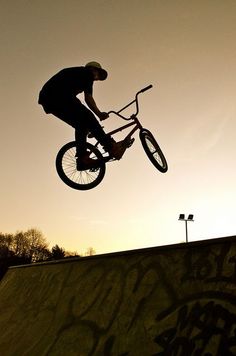 a man riding a bike up the side of a skateboard ramp in the air