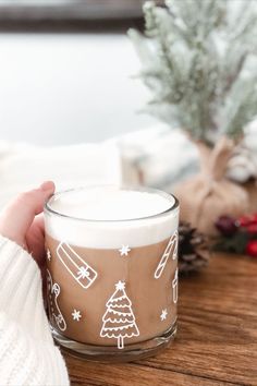 Glass mug with white holiday designs all around sits on wooden bar with open book and holiday decor in back. Holiday designs on mug showing are: Christmas tree, present, gingerbread man, candy cane. Santa Stocking Ideas, Painted Wine Glasses Christmas, Early Morning Coffee, Christmas Cups, Diy Christmas Decorations Easy, Mug Handmade, Holiday Coffee, Painted Wine Glasses, Fresh Coffee