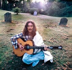 a man with long hair sitting on the ground holding a guitar in front of him