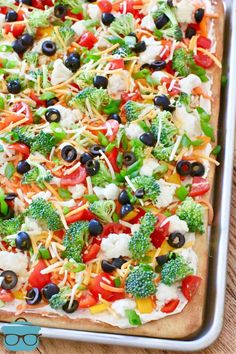 an uncooked pizza with broccoli, olives, cheese and tomatoes