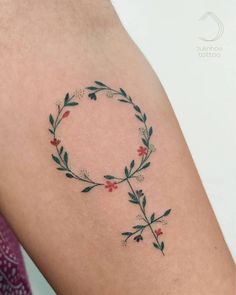 a woman's arm with a tattoo on it that has flowers and leaves in the shape of a circle