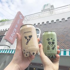 two people holding up cans in front of a building