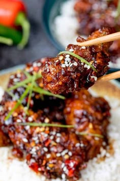 the meat is being served with chopsticks on top of rice and garnished with sesame seeds