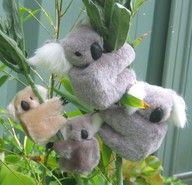 four stuffed koalas are hanging from a tree with green leaves and flowers in the foreground