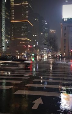 a city street at night with traffic lights and buildings in the background on a rainy day