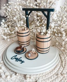 two wooden barrels with wedding rings are on a white table next to some flowers and branches