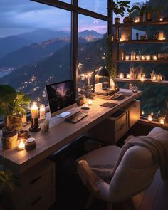 a desk with a computer and candles on it in front of a window overlooking the mountains