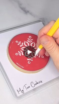 a hand holding a yellow marker near a red doughnut with white designs on it